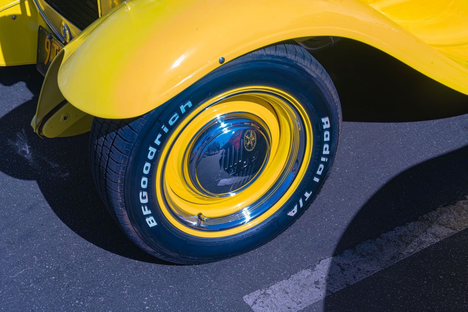 Close-up of a yellow classic car's BFGoodrich Radial T/A tire with a chrome hubcap on pavement.