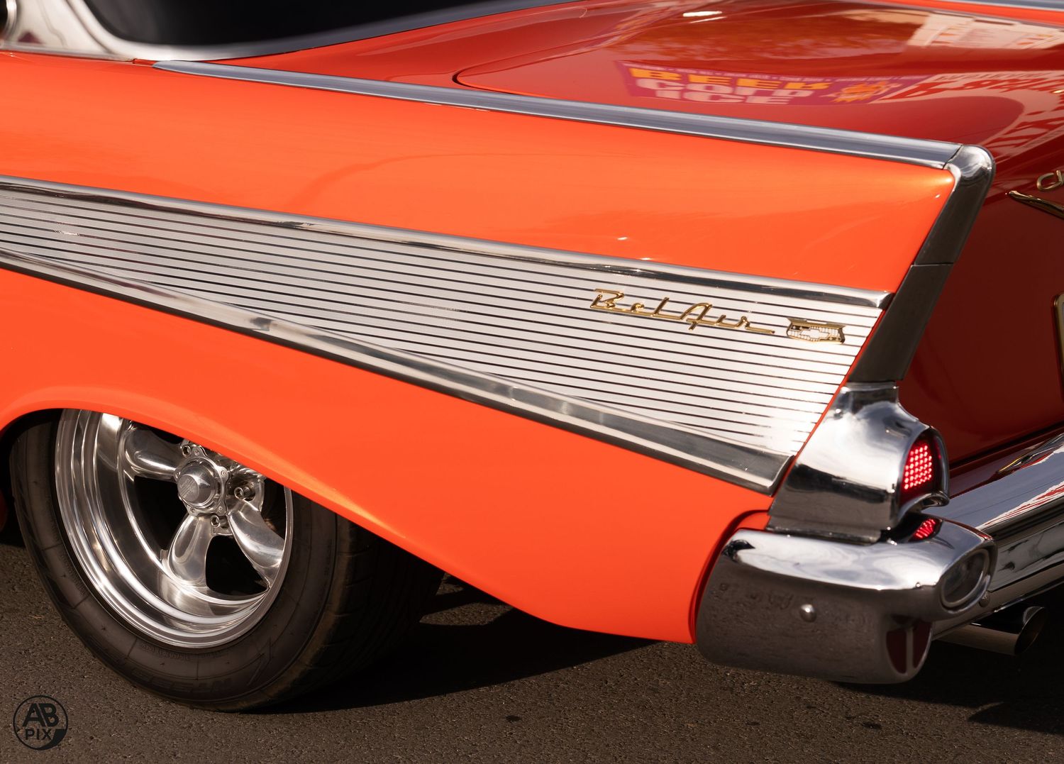 Detail shot of an orange 1957 Chevrolet Bel Air tail fin with chrome trim and custom polished wheel.