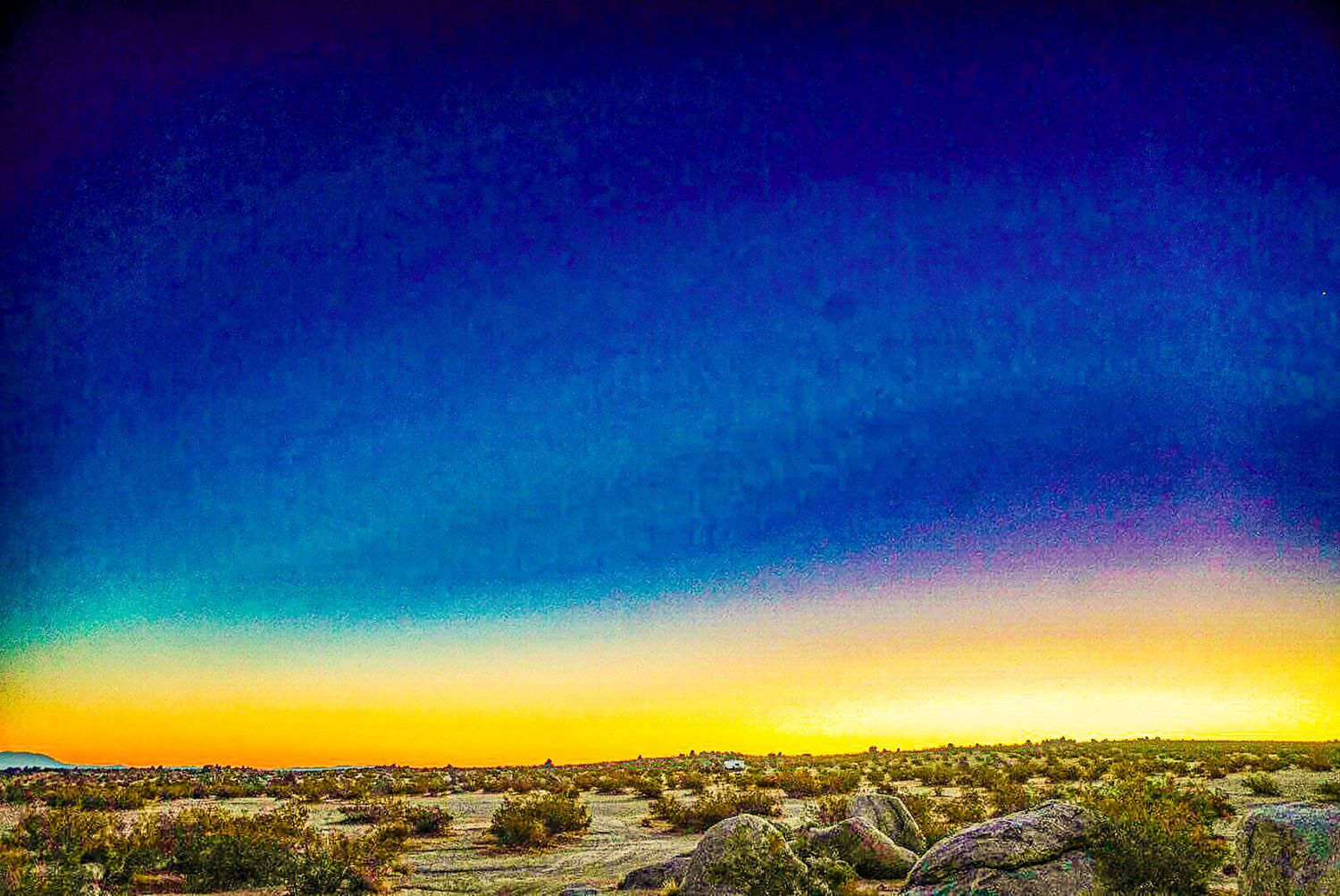 Vibrant desert sunset with deep blue sky transitioning to golden yellow hues over rocky landscape.