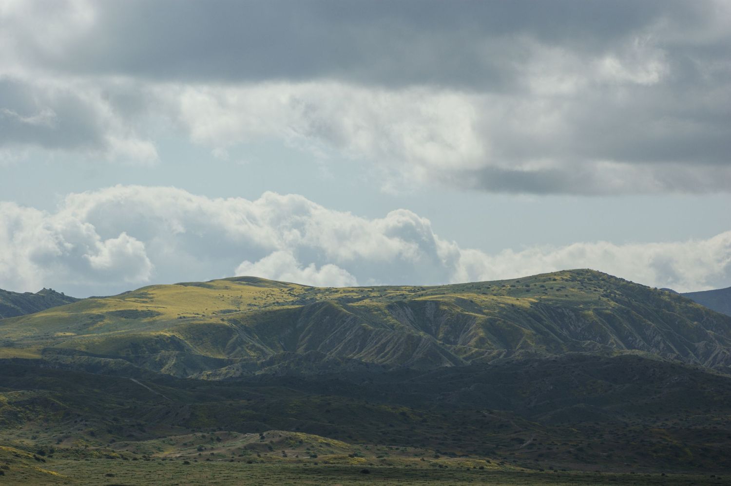 Green rolling hills under dramatic cloudy sky in a scenic mountain landscape.