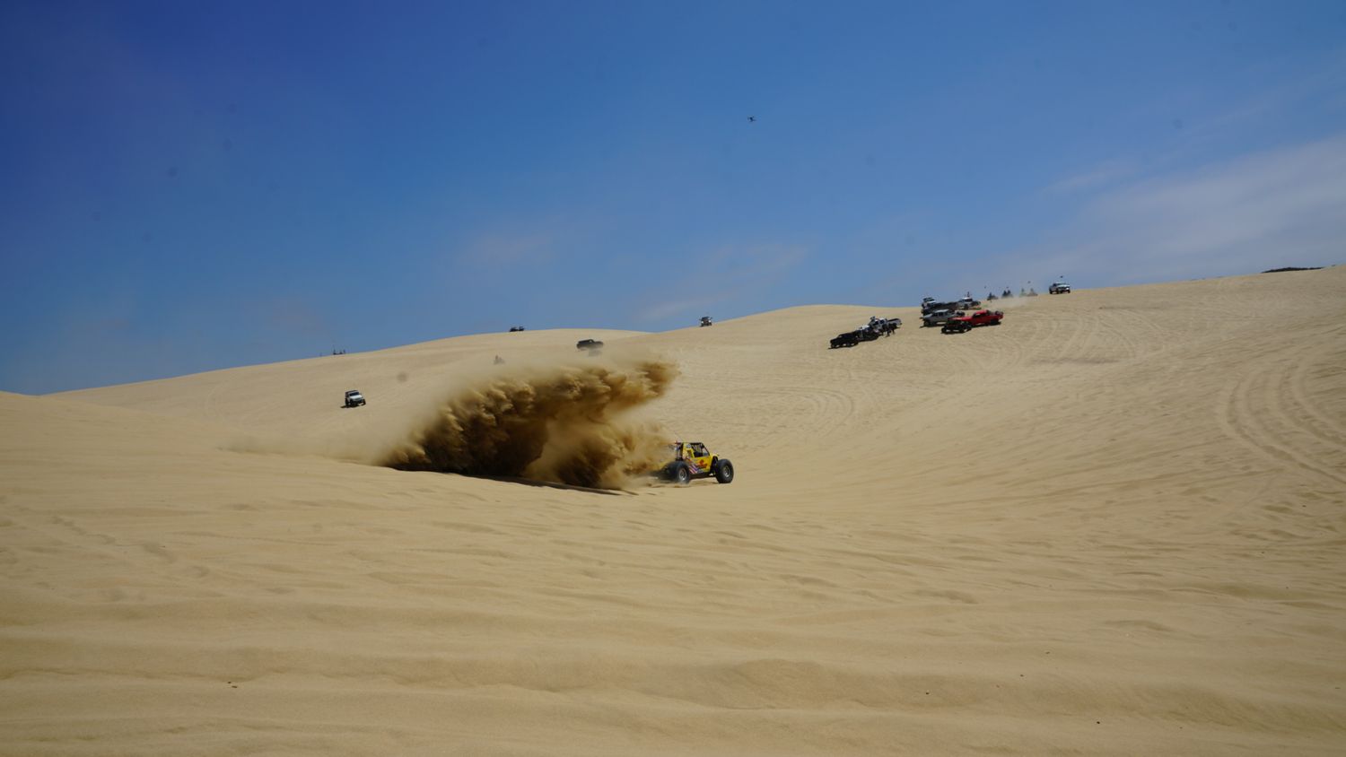 Off-road buggy kicking up a massive dust cloud while racing across expansive desert sand dunes.