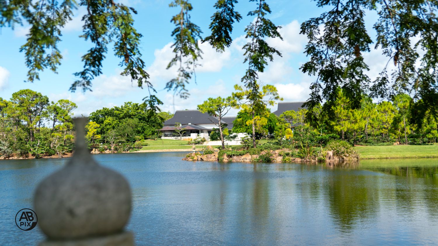 Blurred stone lantern framing a peaceful lake and Japanese garden pavilion.