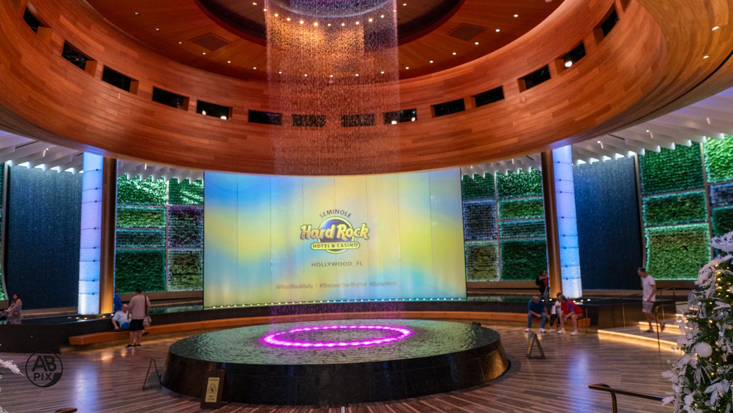 Grand circular hotel lobby with large LED screen, living green walls, and wooden ceiling details.
