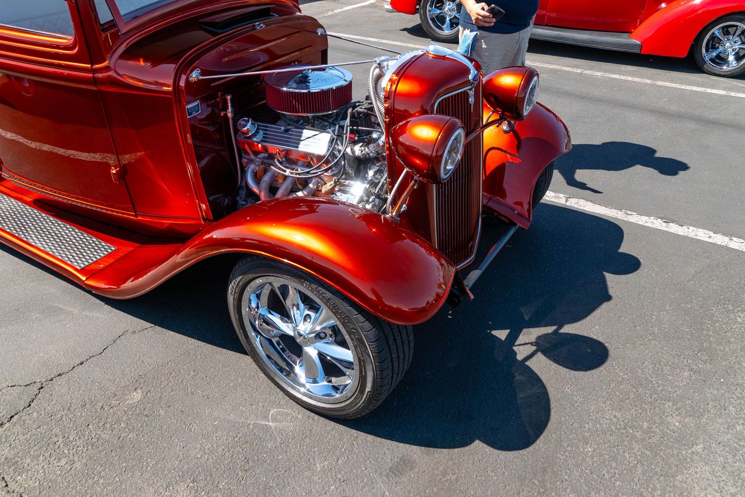 Side view of a candy red 1930s Ford hot rod with exposed supercharged engine and chrome exhaust pipes.