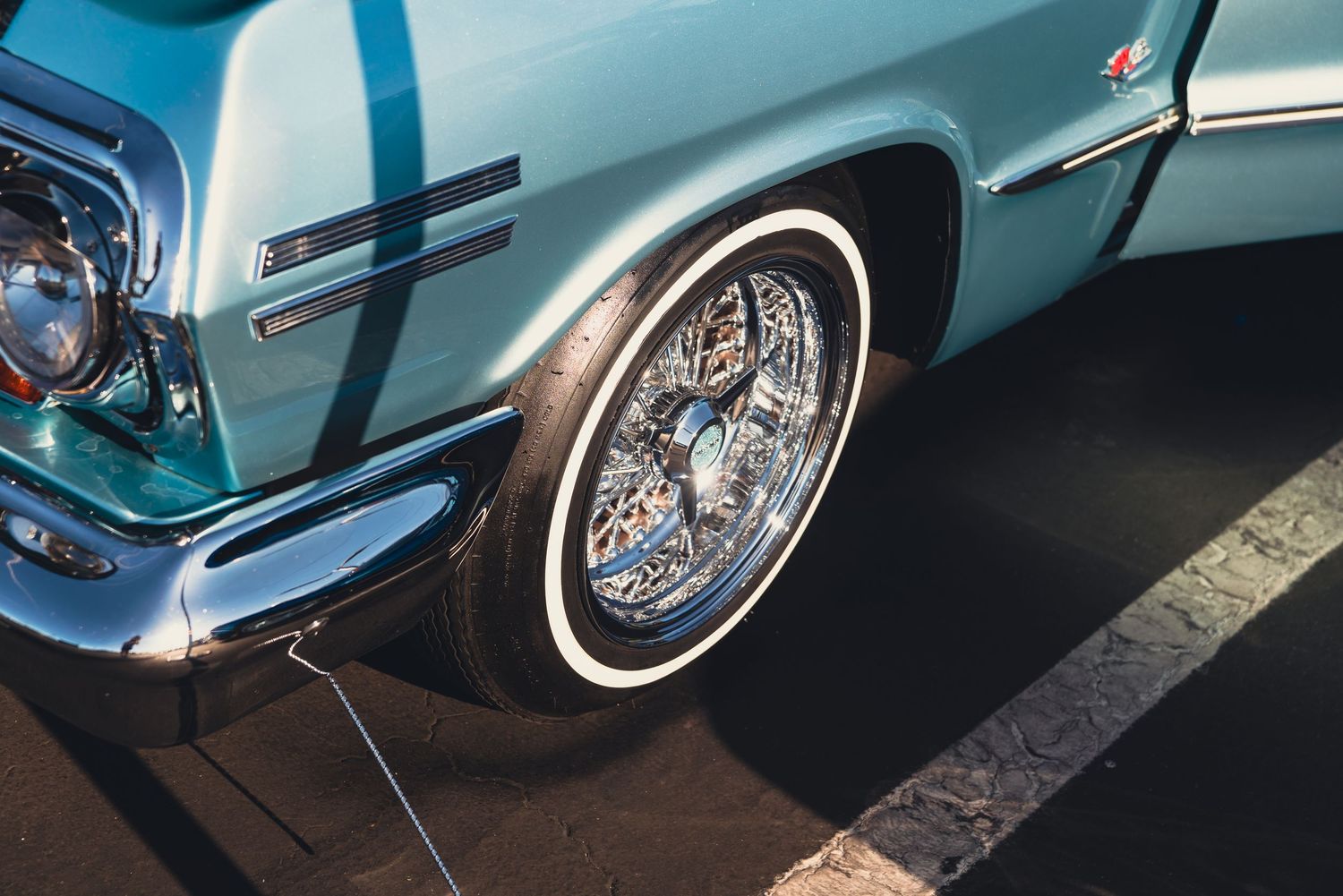Vintage light blue classic car with chrome wire wheels and white wall tires parked on asphalt at a car show.