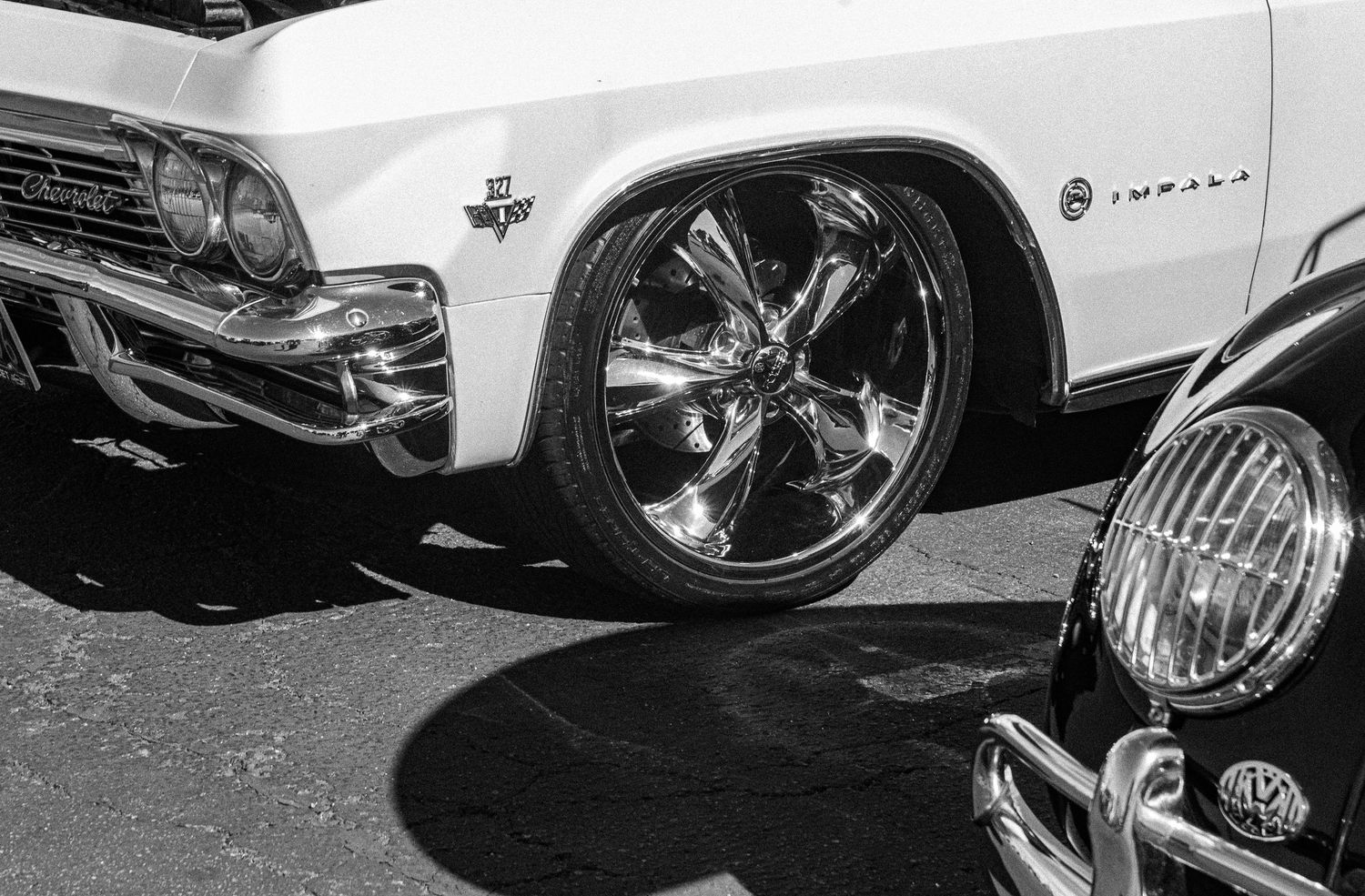 Black and white photo of a classic Chevrolet Impala with chrome wheels at a car show.