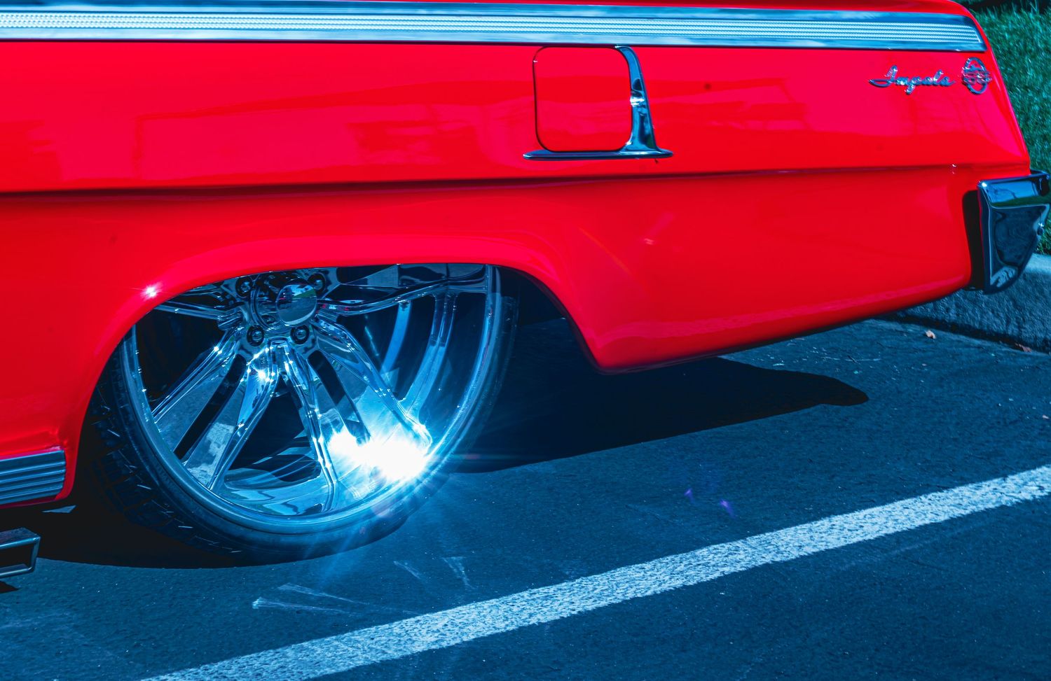 Lowered red classic Chevrolet Impala with chrome wheels and blue underglow lighting on pavement.