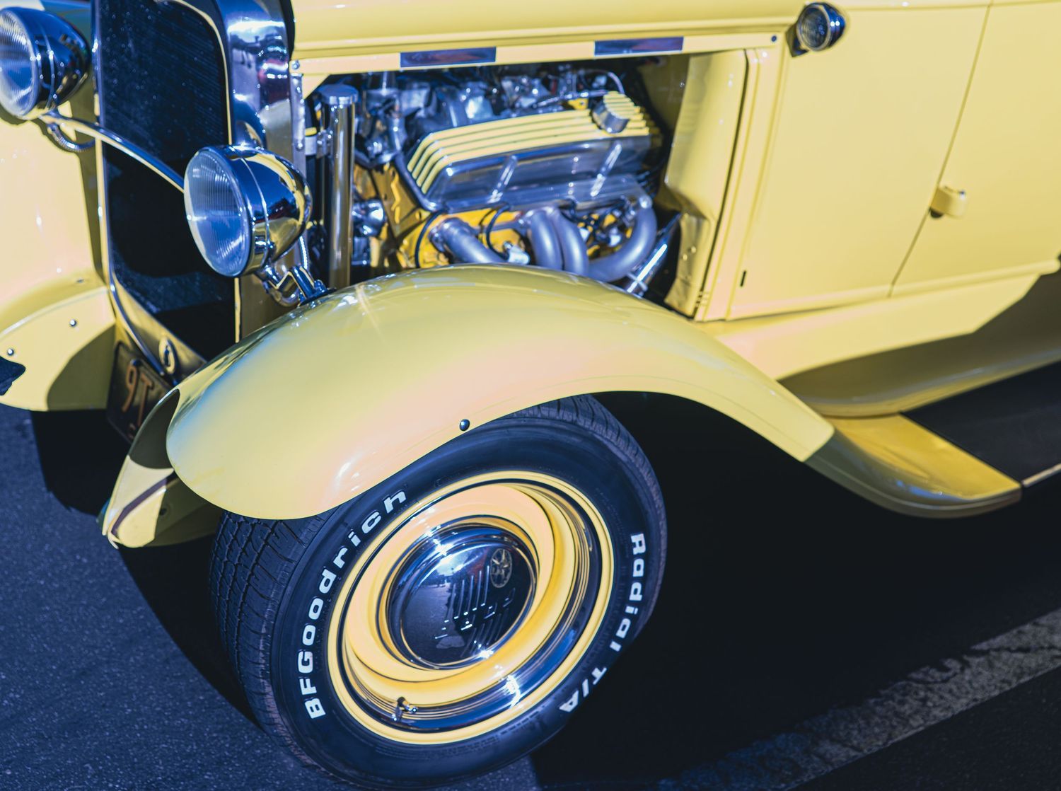 Yellow hot rod classic car with exposed chrome engine and BFGoodrich whitewall tire on fender.
