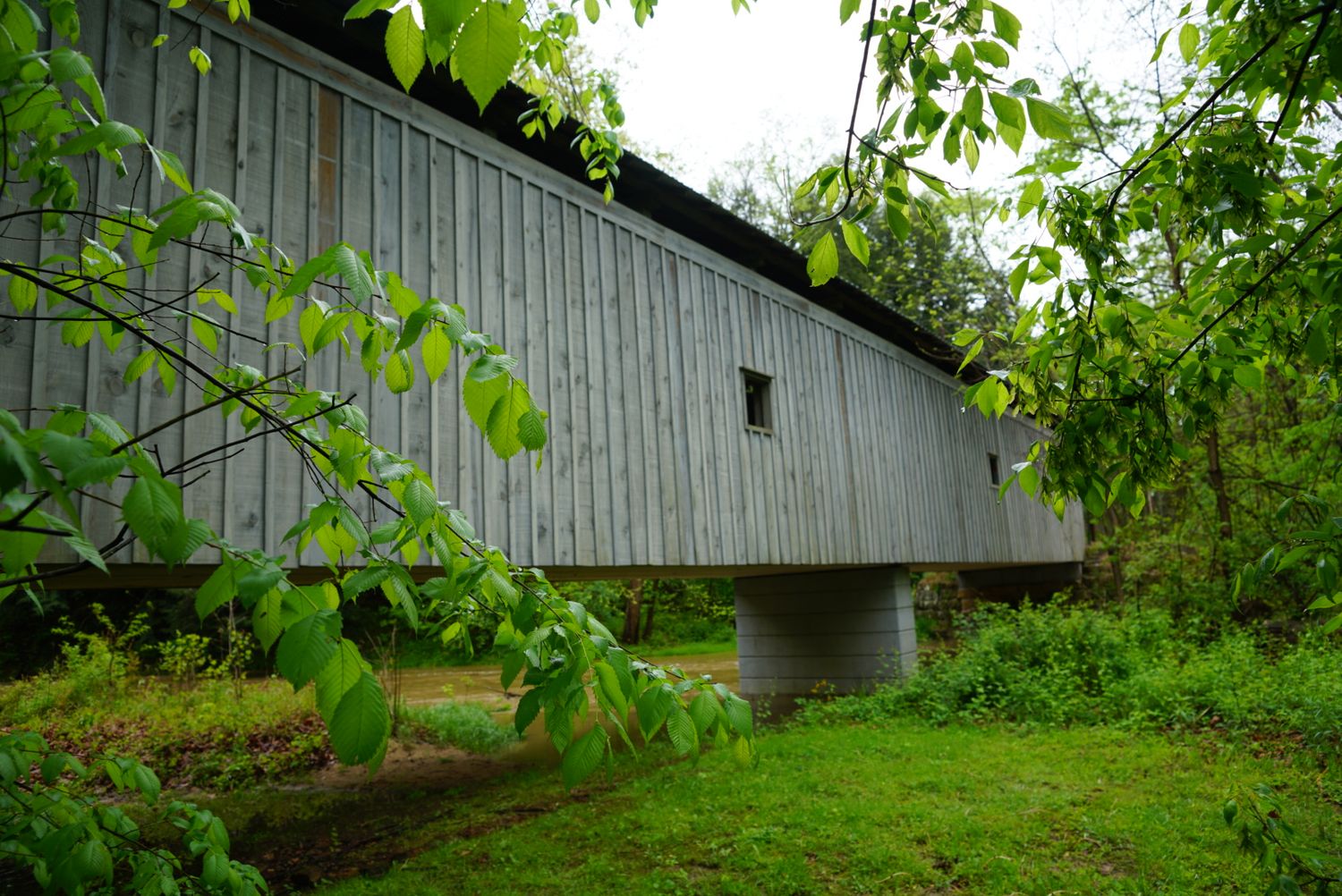 A historic gray wooden covered bridge surrounded by lush green trees and foliage.