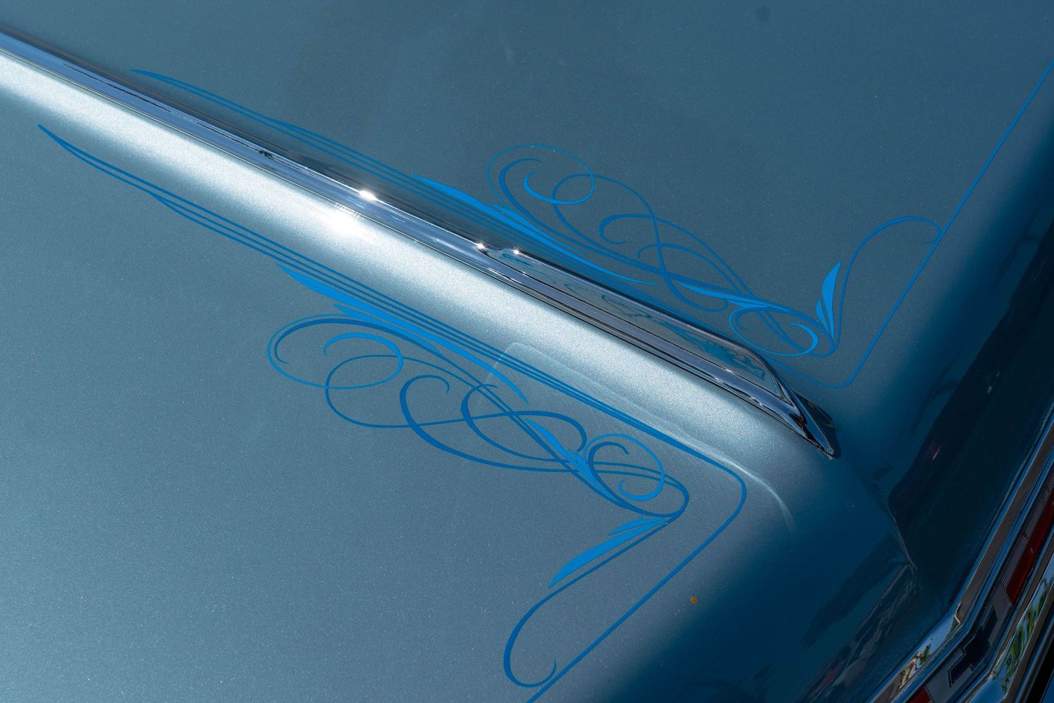 Detail of a light blue classic car hood featuring elegant hand-painted blue pinstripe scroll artwork.