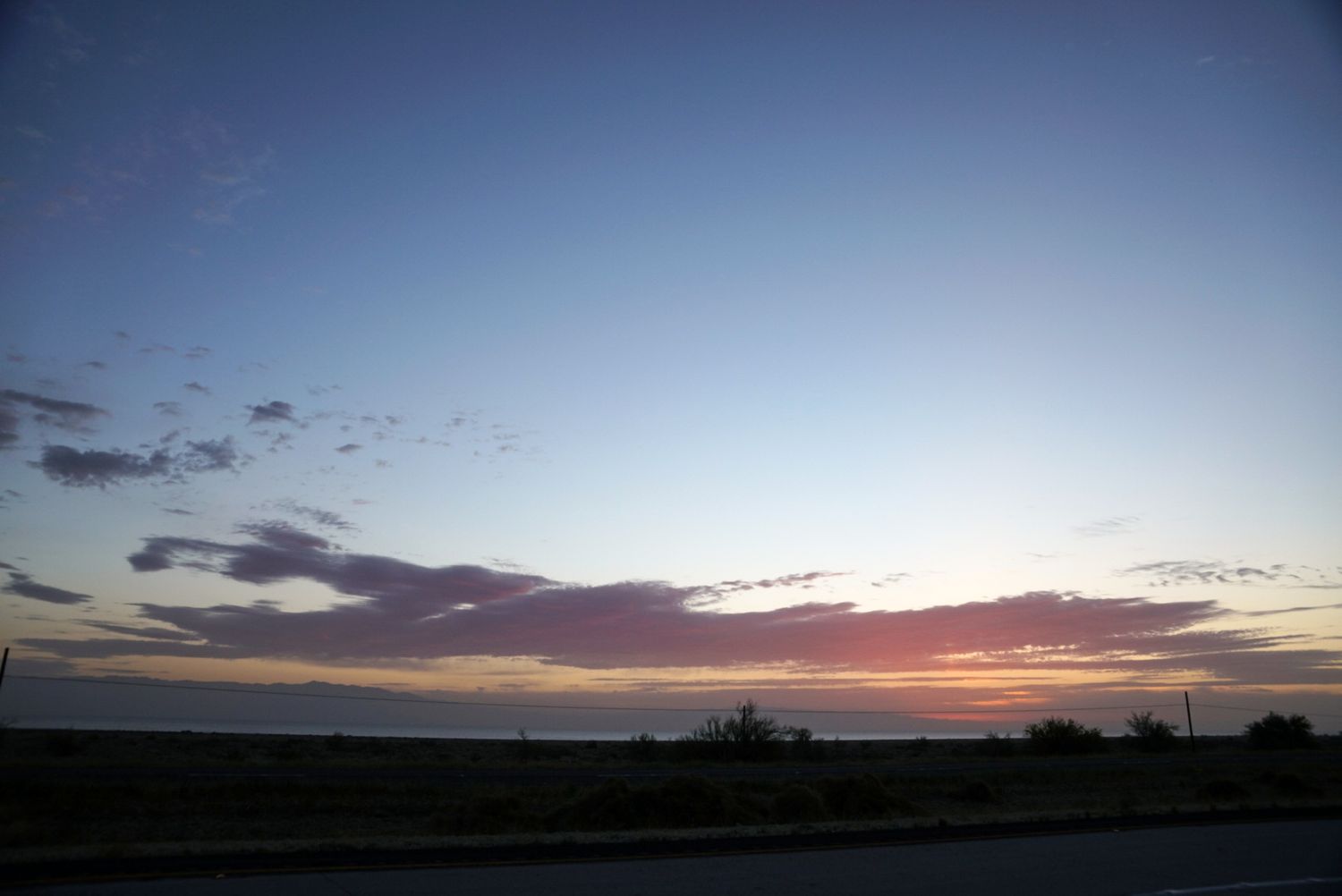 Colorful sunset over a calm ocean horizon with pink and purple clouds against a deep blue twilight sky.