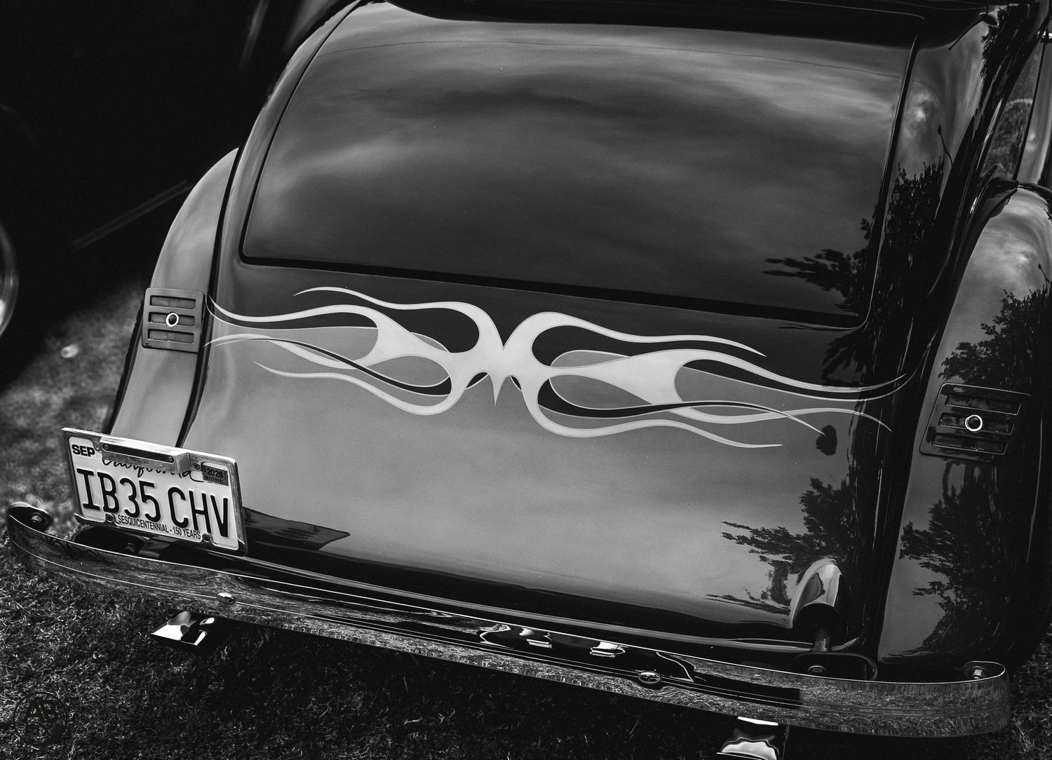 Black and white photo of classic car trunk with flame graphics and vintage license plate.