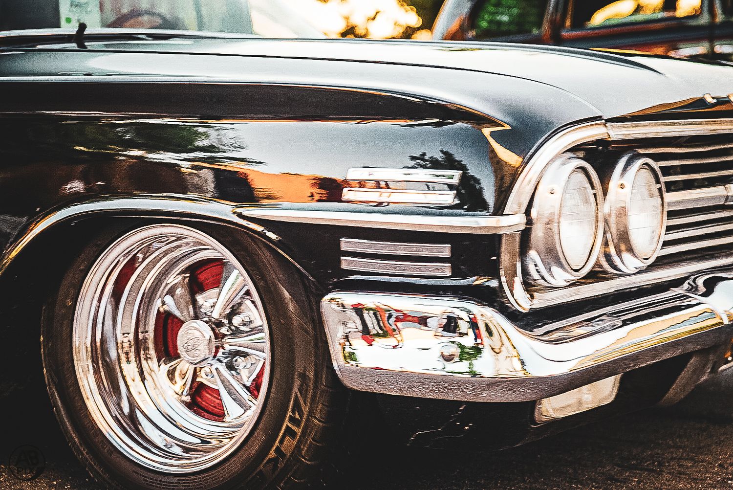 Close-up of a shiny black classic vintage car front end with chrome trim and red wheel.