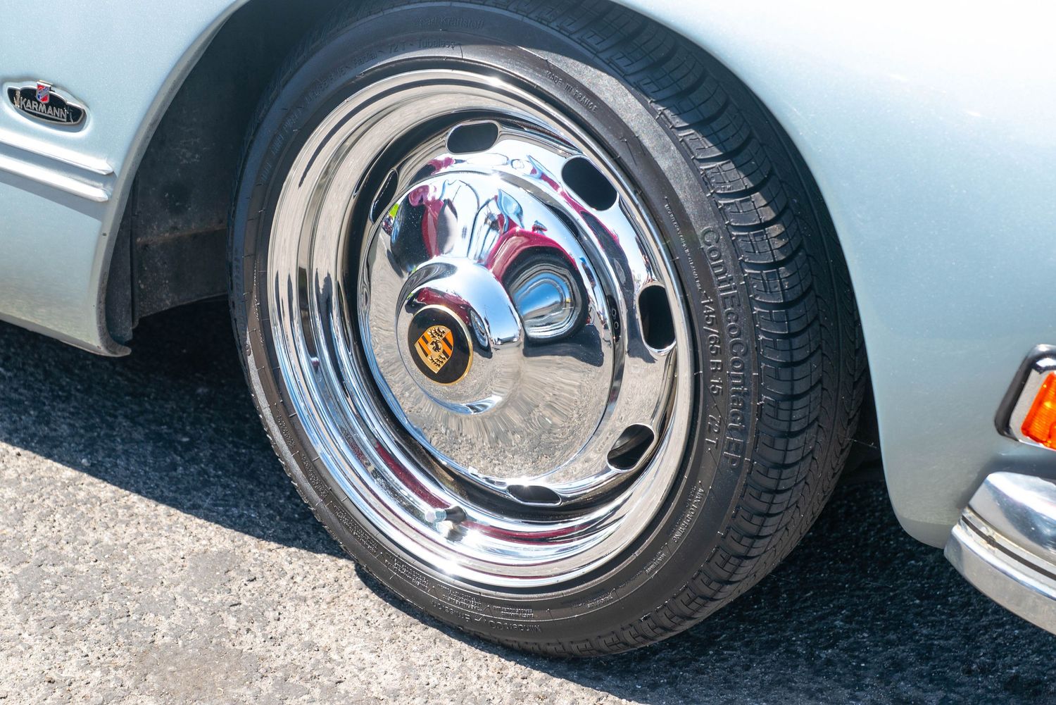 Shiny chrome wheel with vintage hub cap on a classic silver lowrider car parked on asphalt.