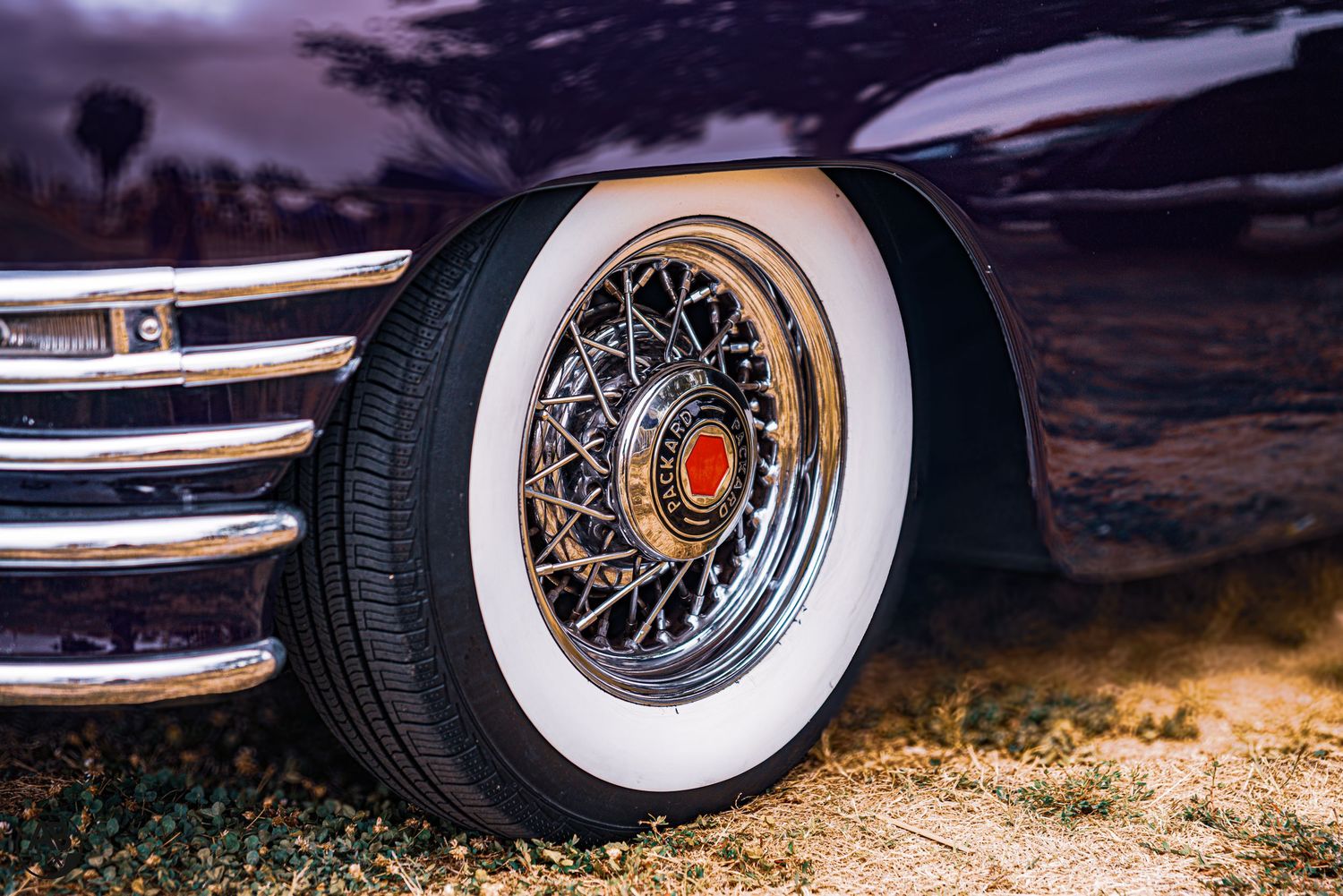 Classic vintage car with chrome wire spoke wheel and white sidewall tire on gravel ground.