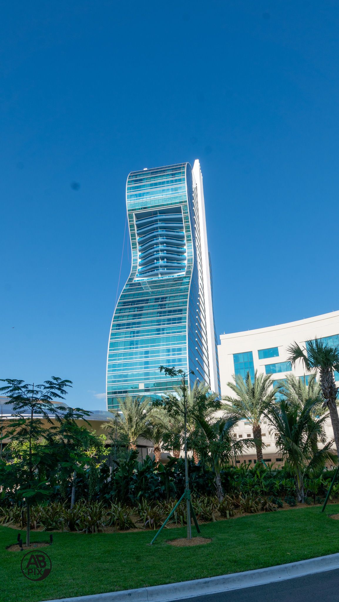 Elegant curved glass hotel tower with wavy facade rising above lush tropical green landscaping.