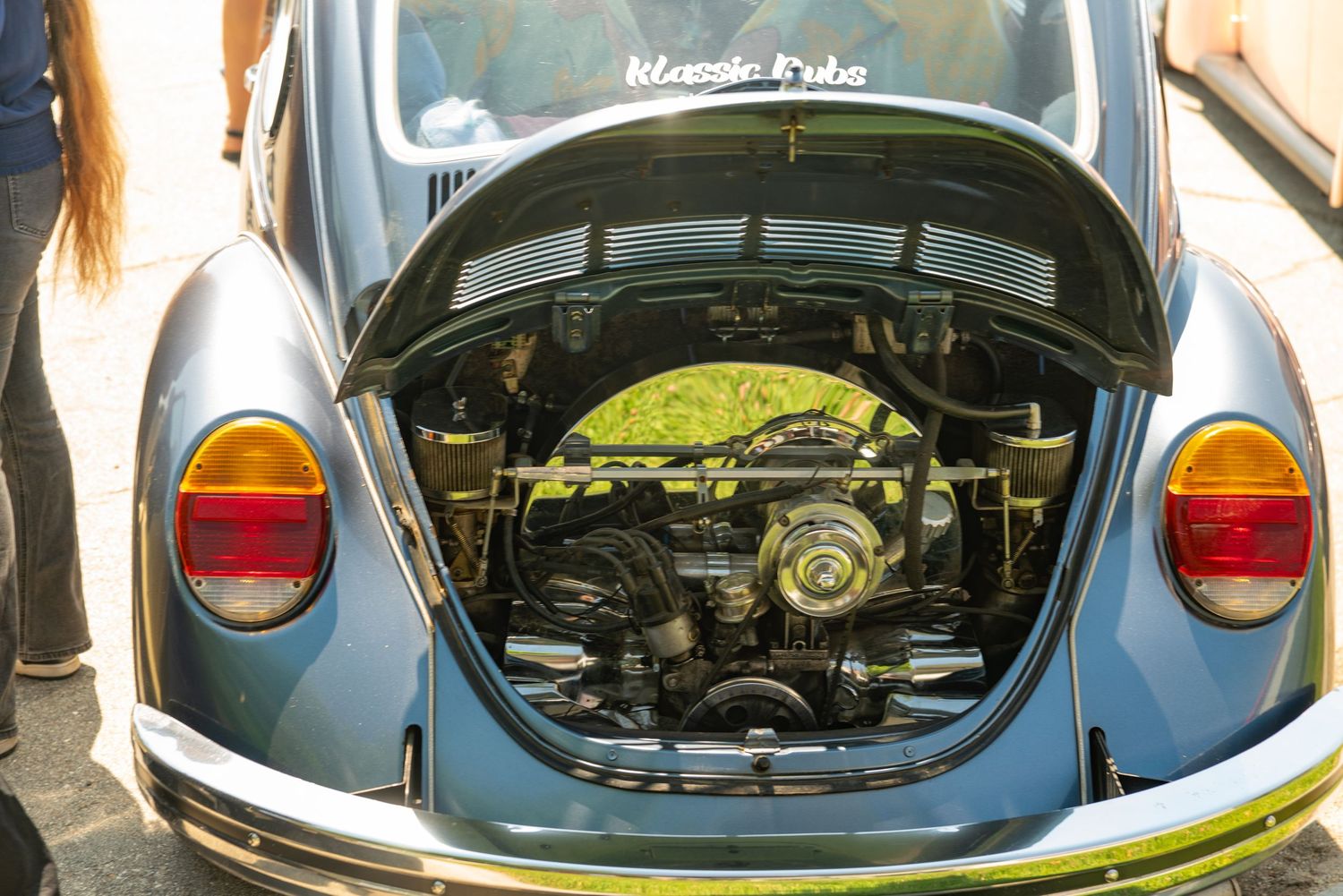 Vintage VW Beetle with open rear engine compartment displaying classic air-cooled engine at a car show.