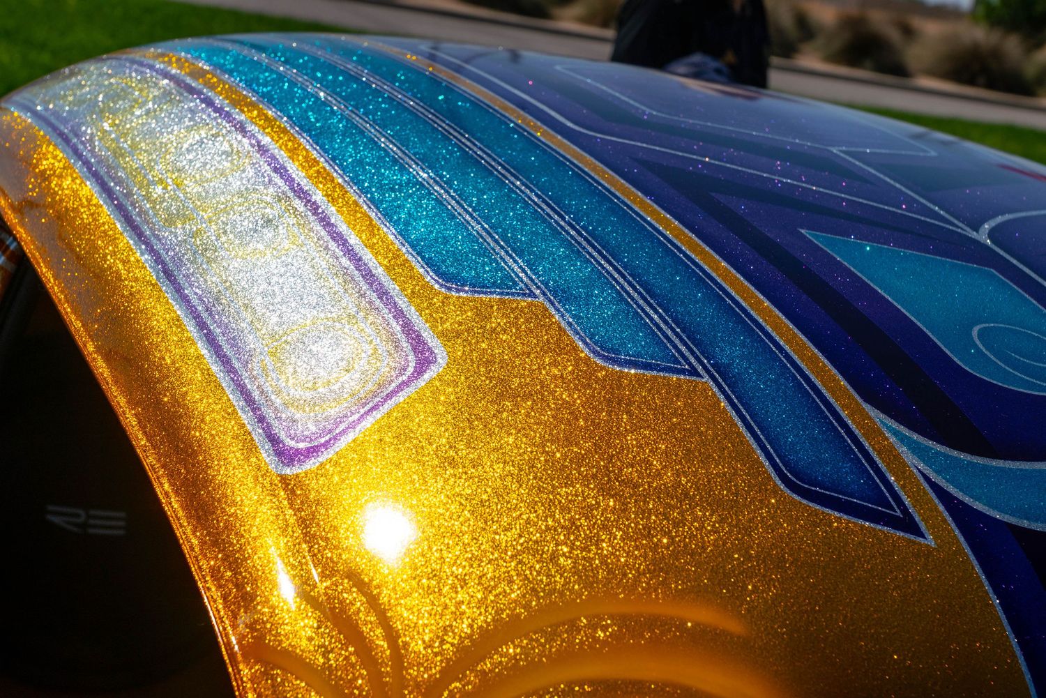 Close-up of a custom car with stunning gold metallic flake paint and blue geometric pinstripe design.