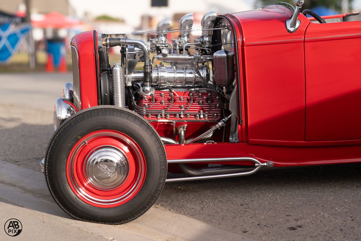 Close-up of a red vintage hot rod roadster with exposed chrome V8 engine and red wheel.