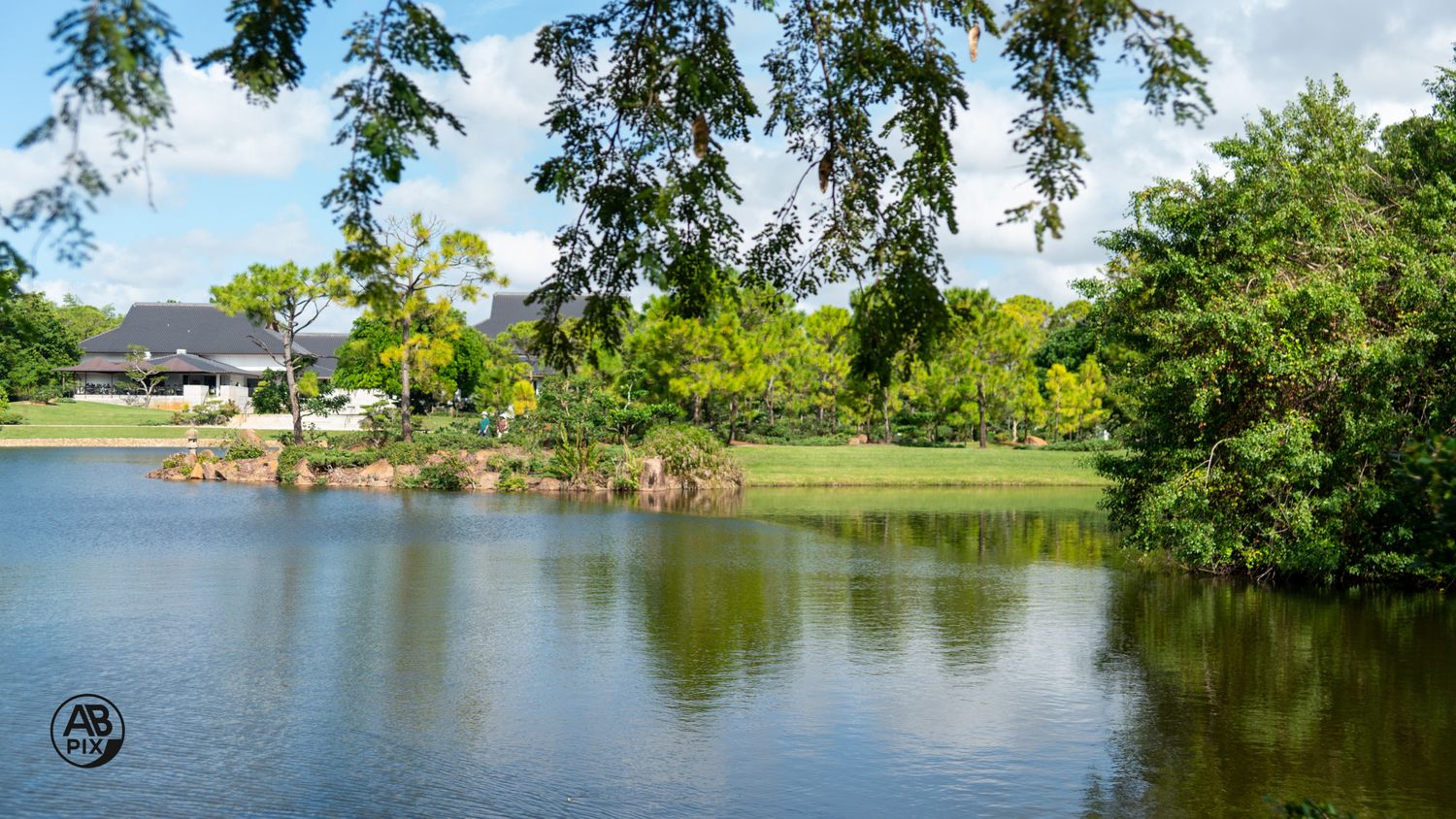 Serene Japanese garden lake reflecting lush green trees and traditional building.