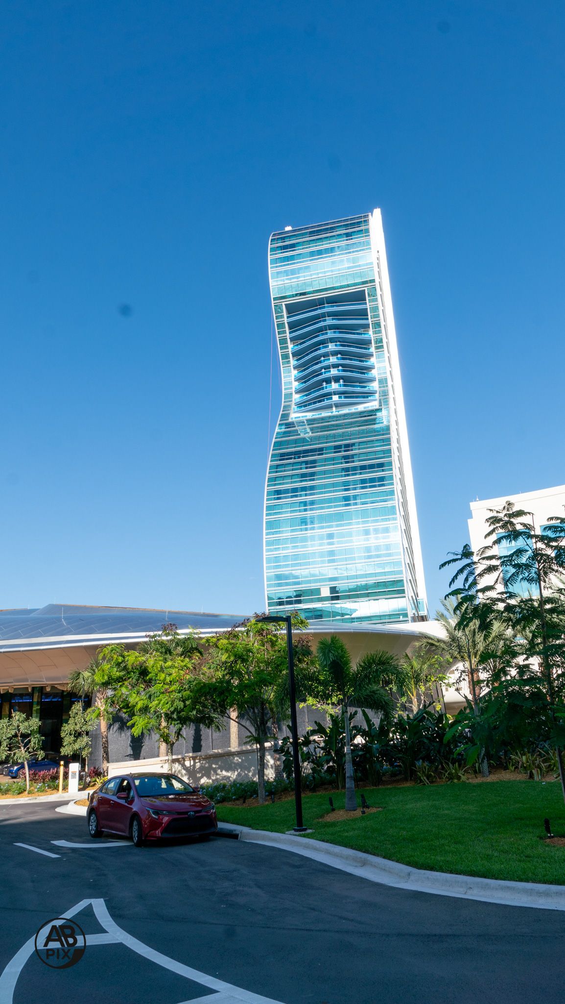 Striking twisted glass tower skyscraper rising against clear blue sky with tropical landscaping.