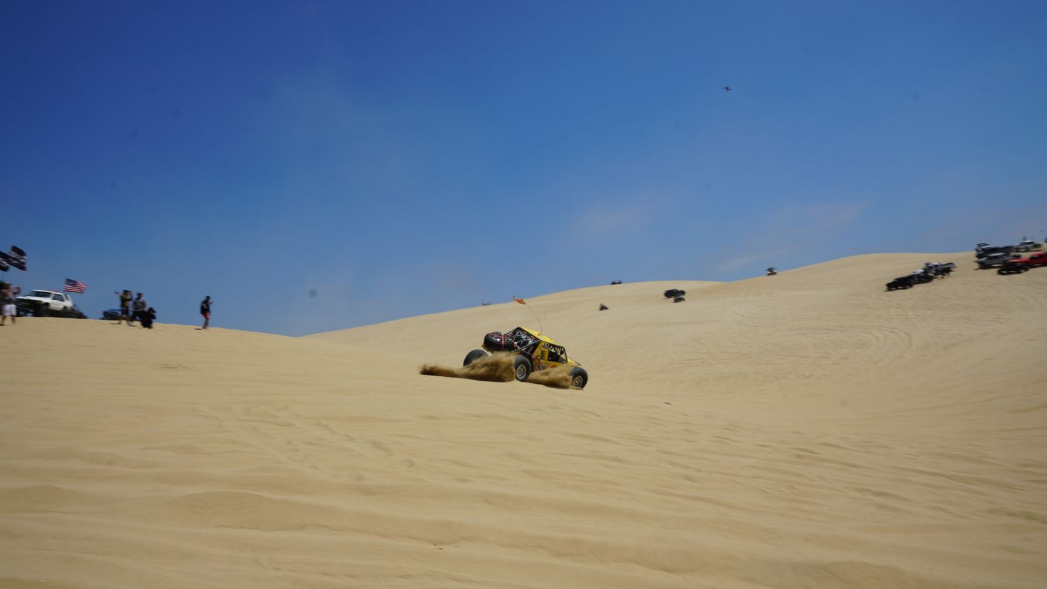 Overturned yellow dune buggy resting on its side on sandy desert dunes after a rollover accident.