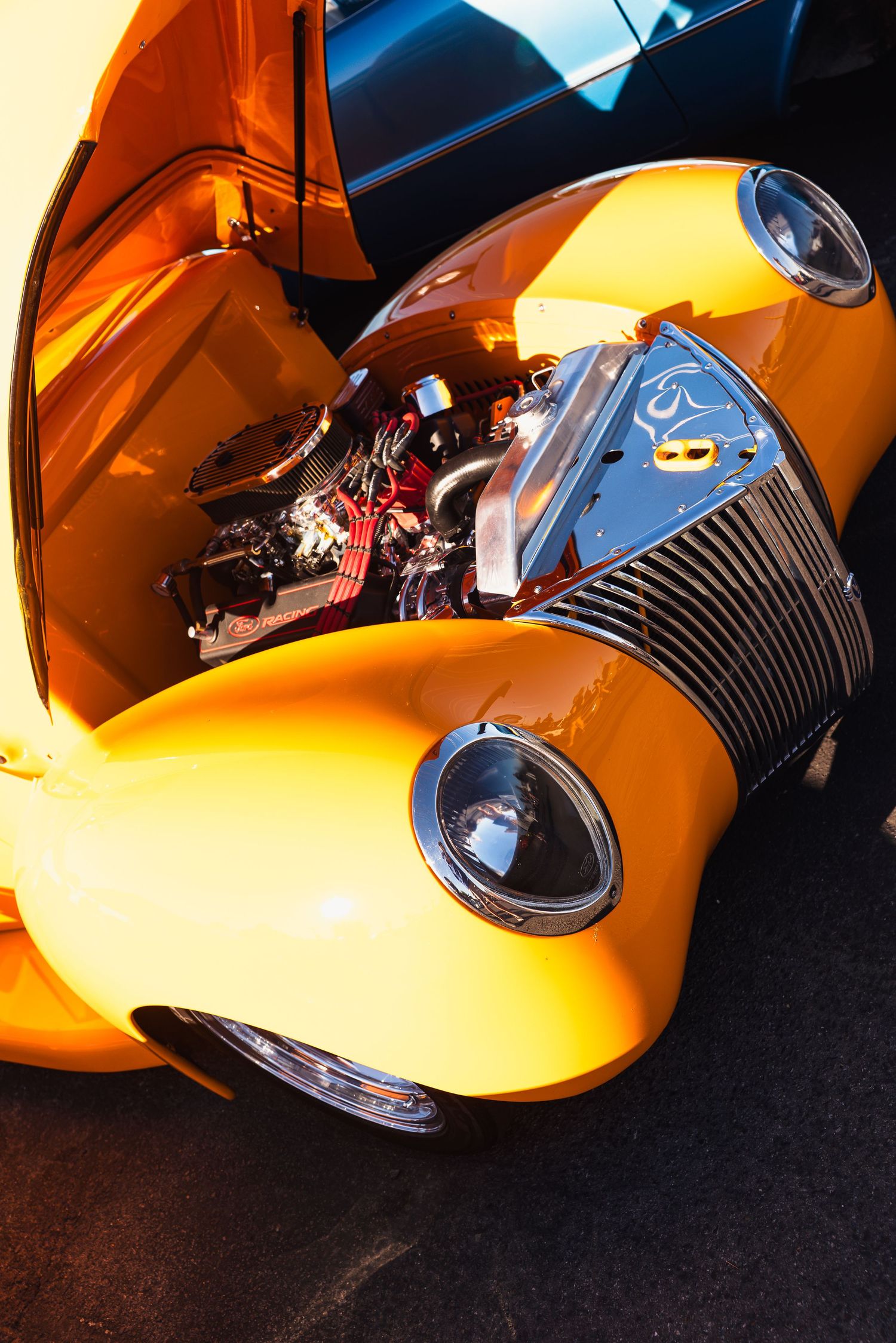 Bright orange custom hot rod with open hood revealing a polished high-performance engine at a car show.