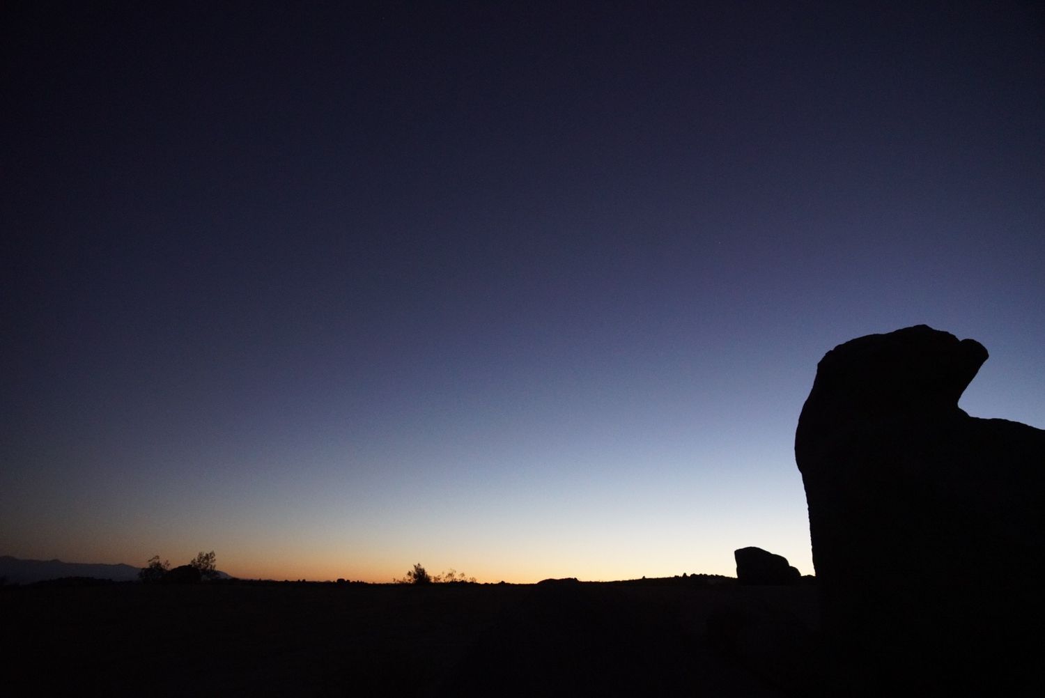 Silhouette of desert rock formation against vibrant orange and blue sunset sky.