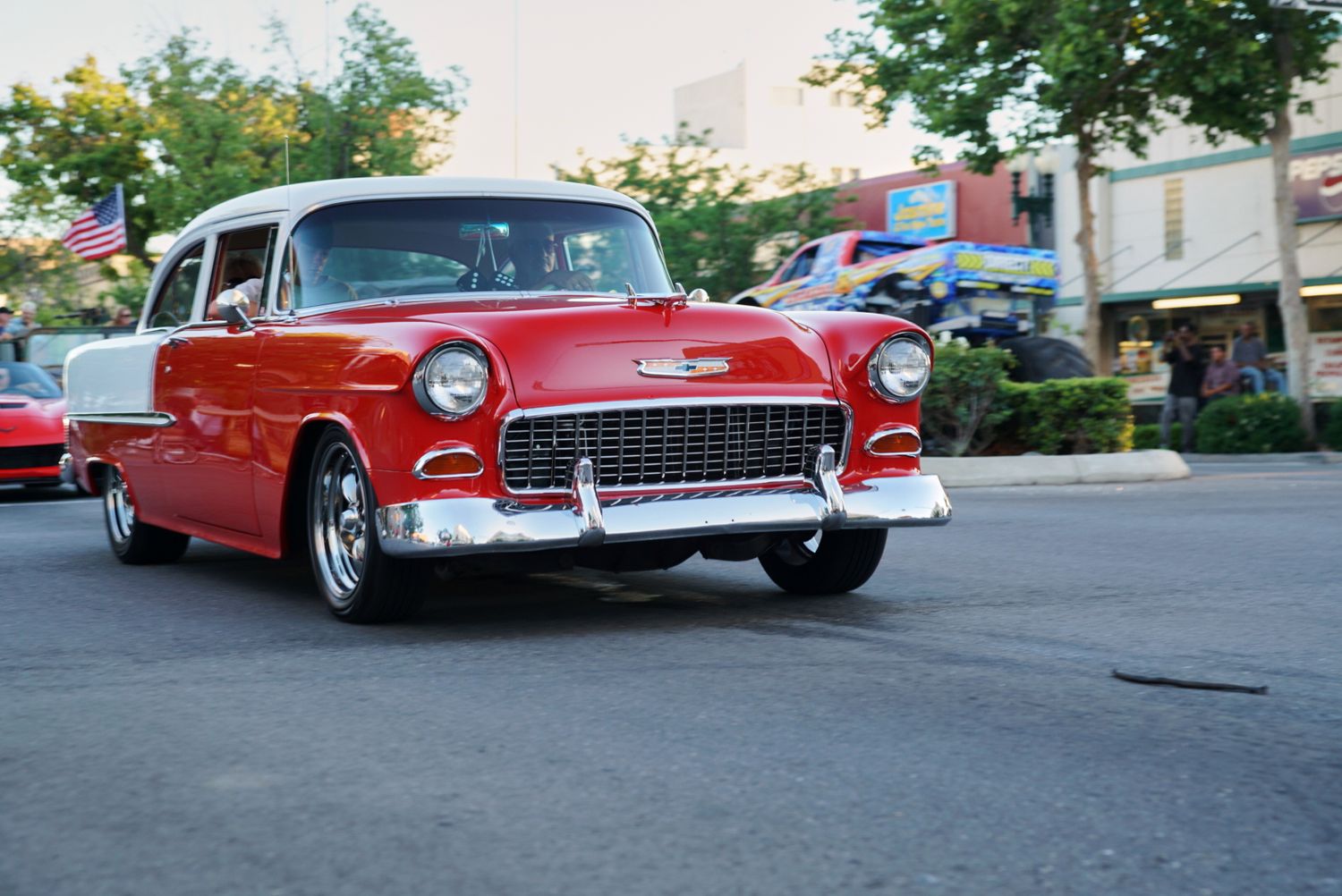 A restored red and white 1955 Chevrolet Bel Air classic car driving on a street at a car show.