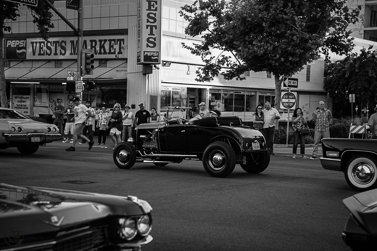 Black and white photo of a classic black roadster hot rod at a street car show.