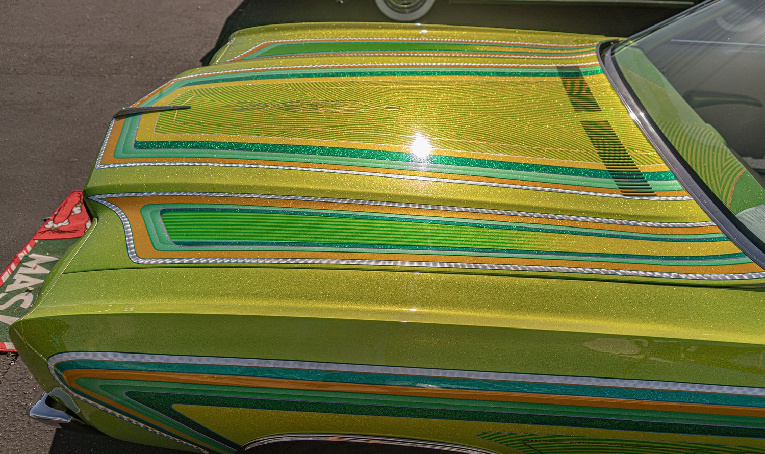 Close-up of a custom green lowrider car hood with vibrant striped paint design and decorative detailing.