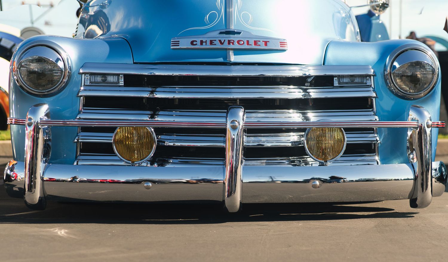 Close-up of a classic chrome Chevrolet truck grille with yellow fog lights at a car show.