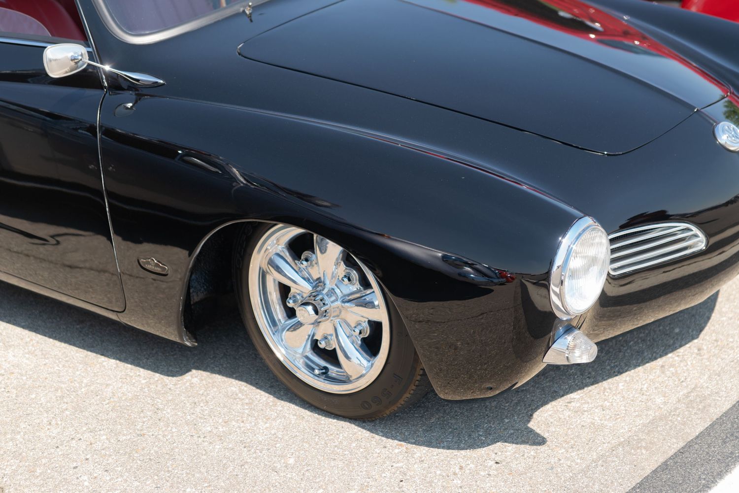 Close-up of a sleek black custom classic car with chrome wheels on display at an outdoor car show.