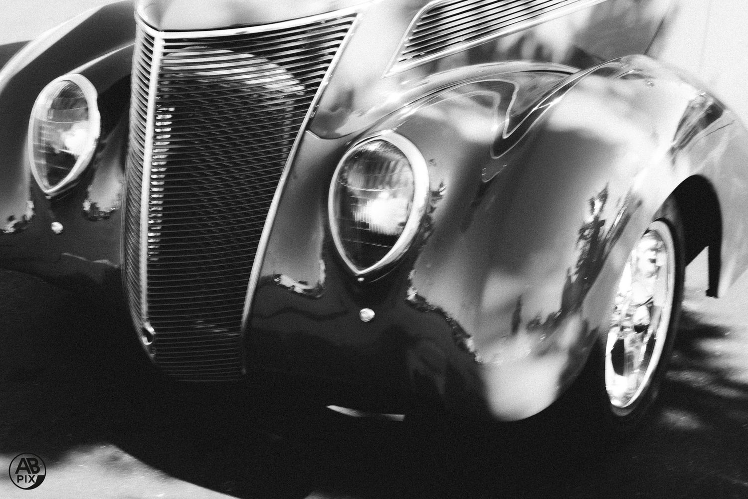 Close-up black and white photo of a classic vintage car front grille and headlight.