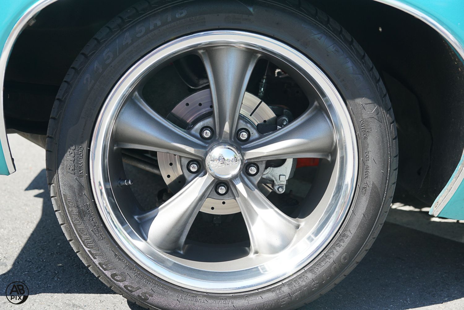 Chrome five-spoke alloy wheel with disc brake on a classic teal vintage car.