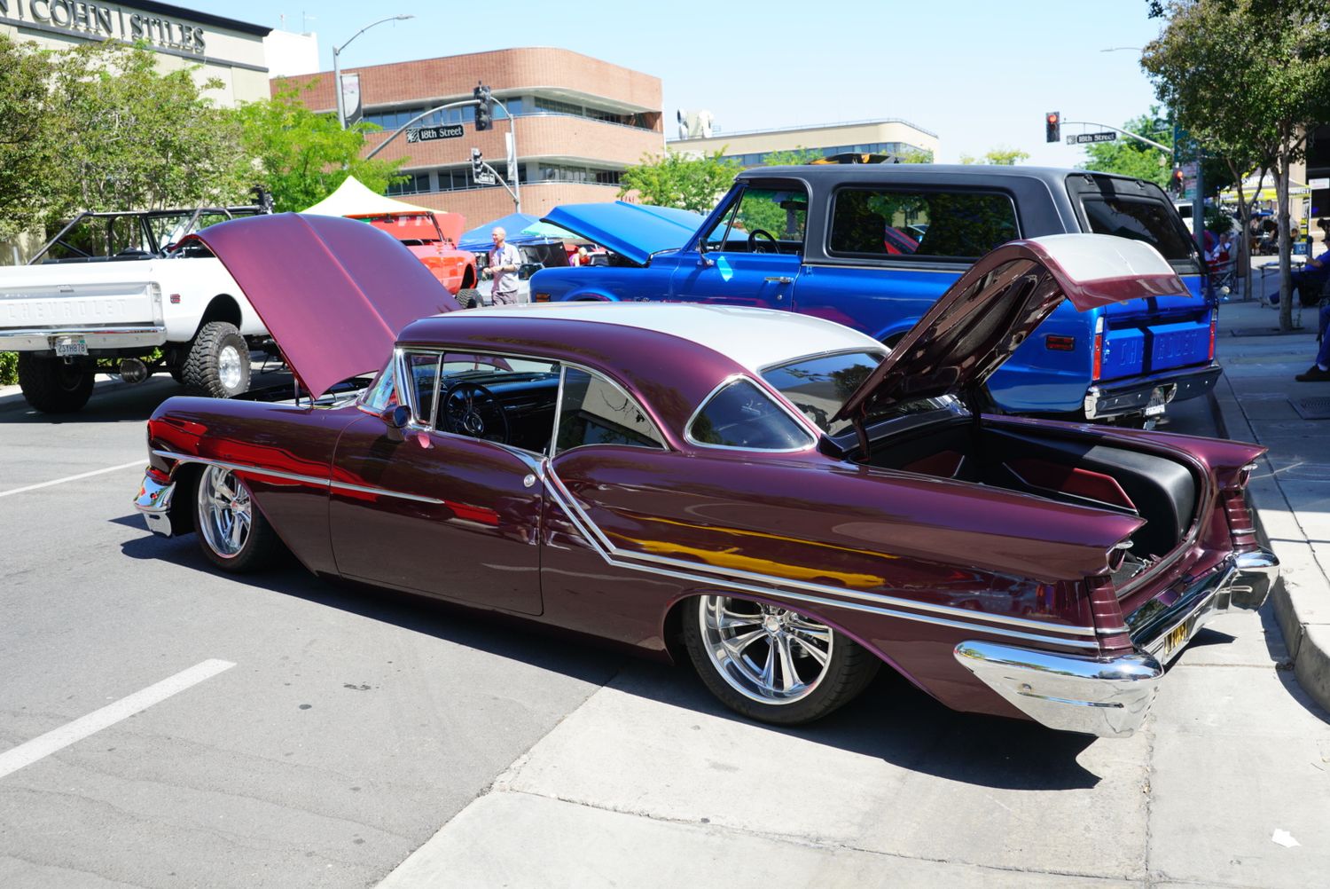 Classic 1950s burgundy lowrider car with hood open at outdoor car show.