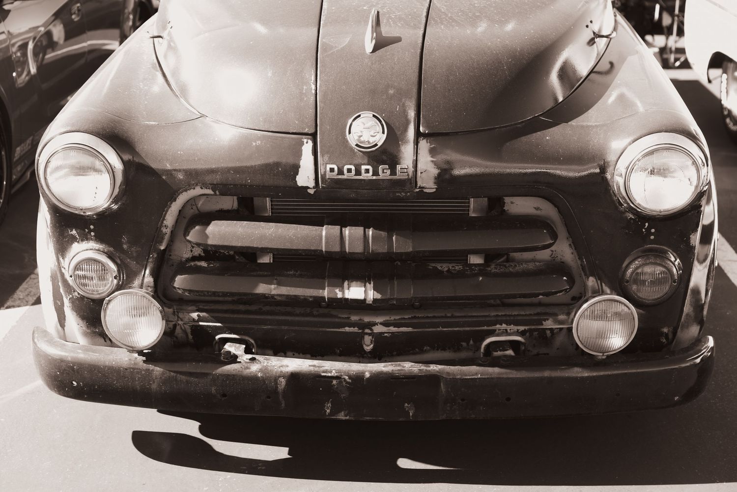 Vintage Dodge truck front grille close-up in sepia tone, showing classic headlights and chrome details.