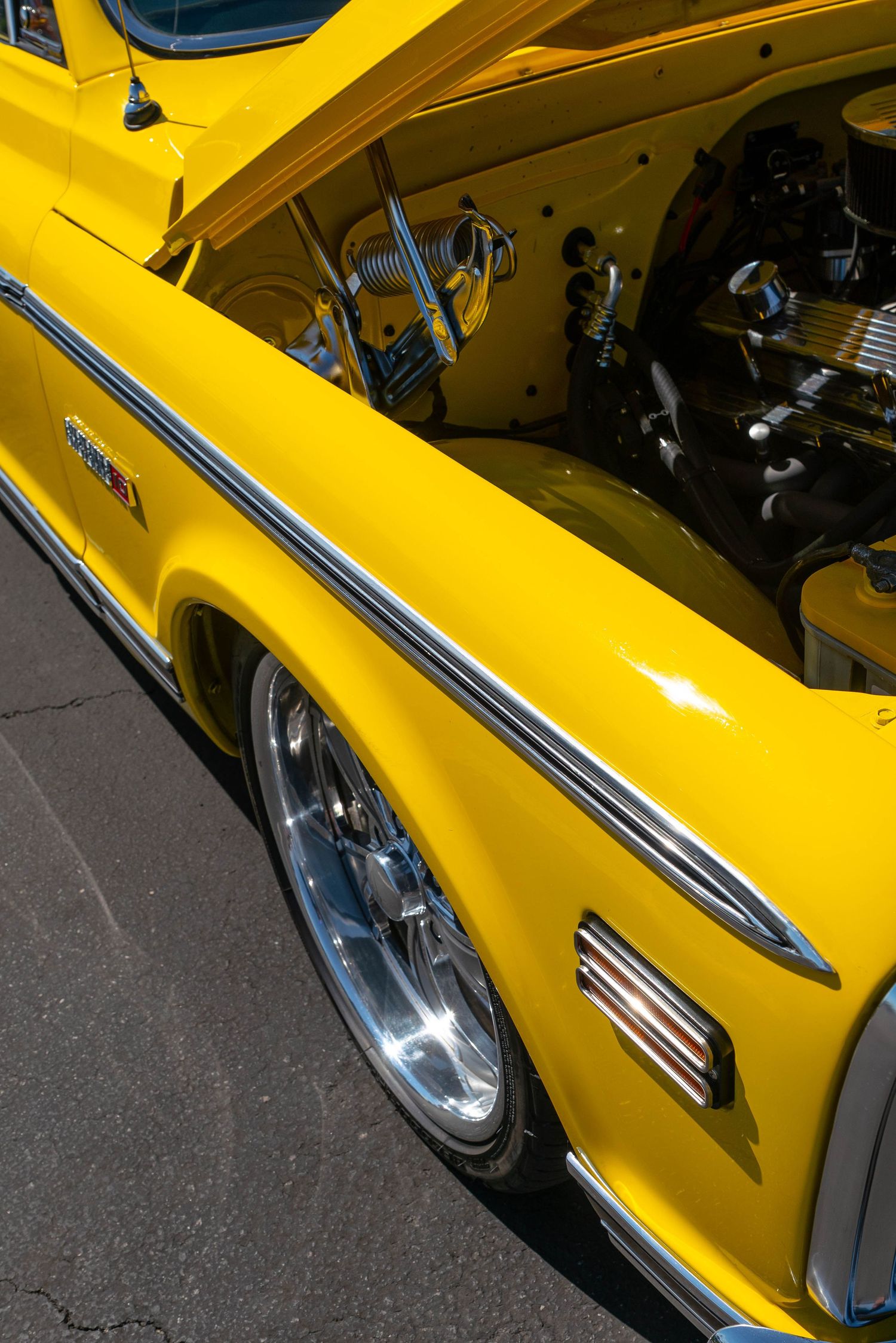 Side view of a bright yellow custom Chevrolet C10 pickup truck with open hood revealing polished engine.