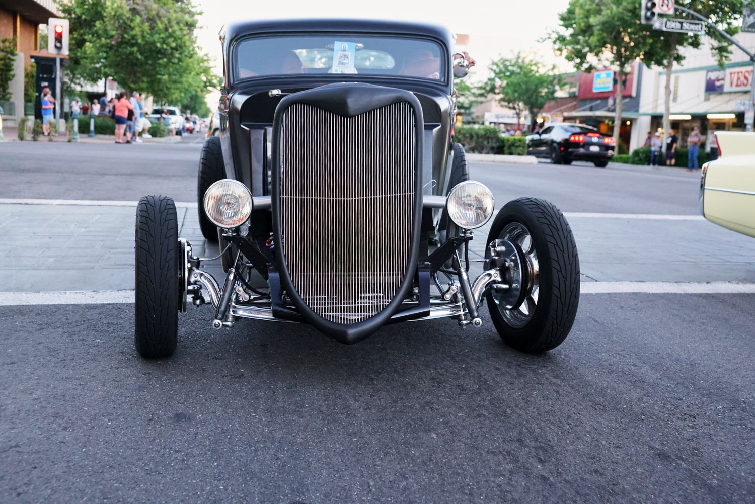 Black 1933 Ford hot rod coupe with vertical grille parked on a downtown street.
