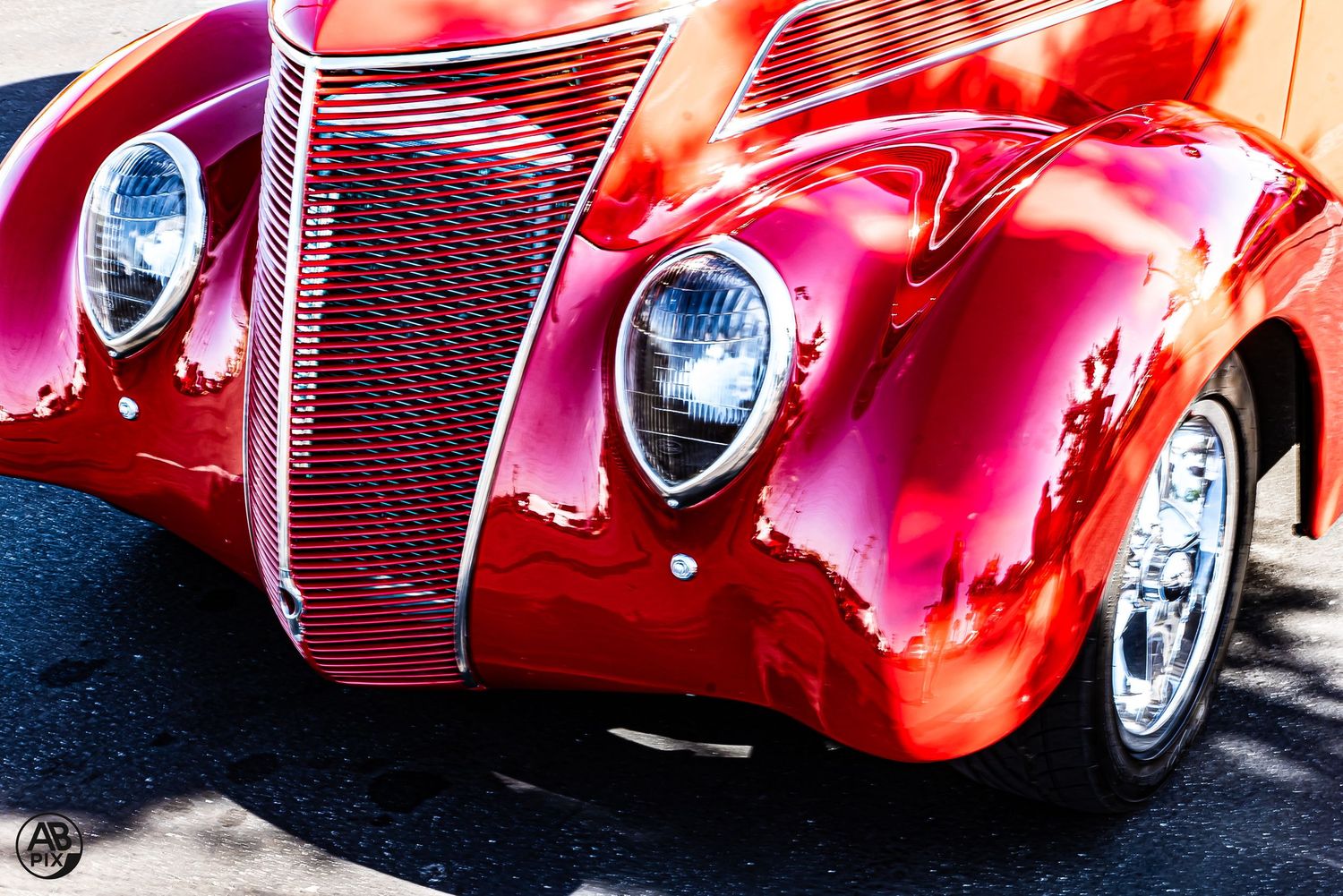 Close-up of a shiny red classic Ford hot rod with teardrop headlights and chrome grille details.