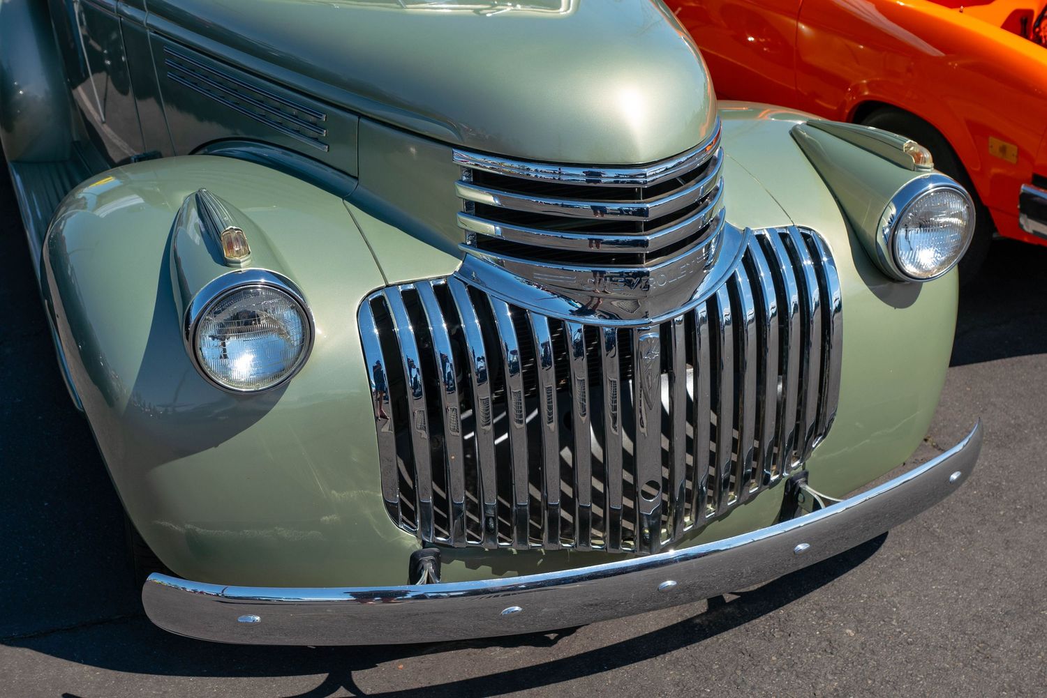 Front view of a restored sage green 1941 Chevrolet with polished chrome vertical bar grille at a car show.