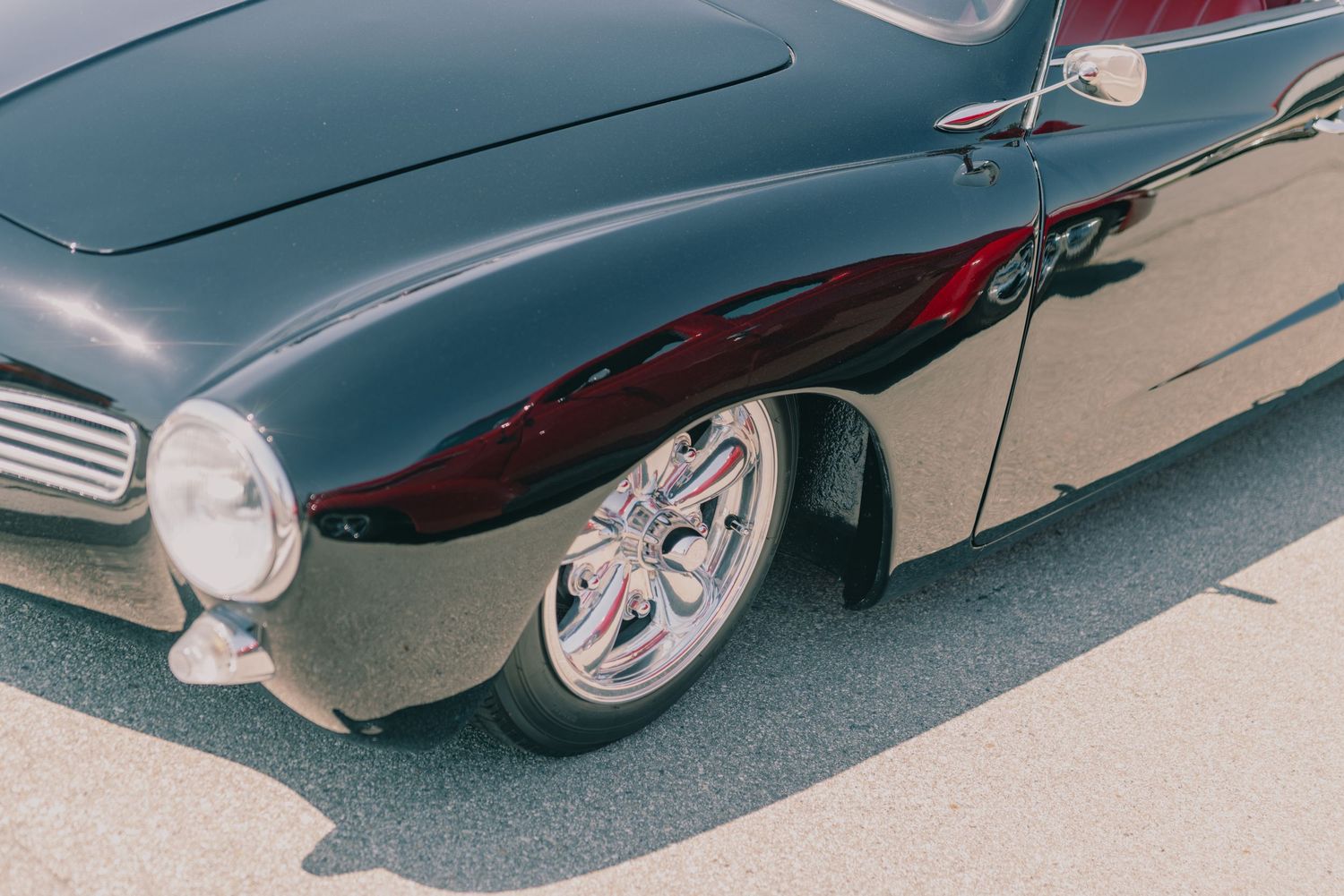 Front wheel detail of a custom black classic car with chrome spoke rims and red brake calipers.