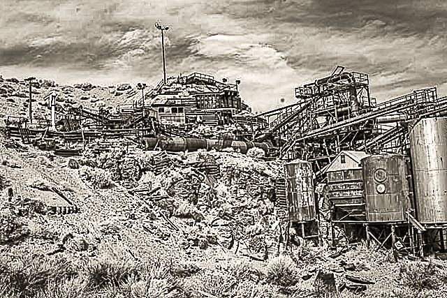 Black and white photo of an abandoned industrial mining complex with rusted equipment and rocky terrain.
