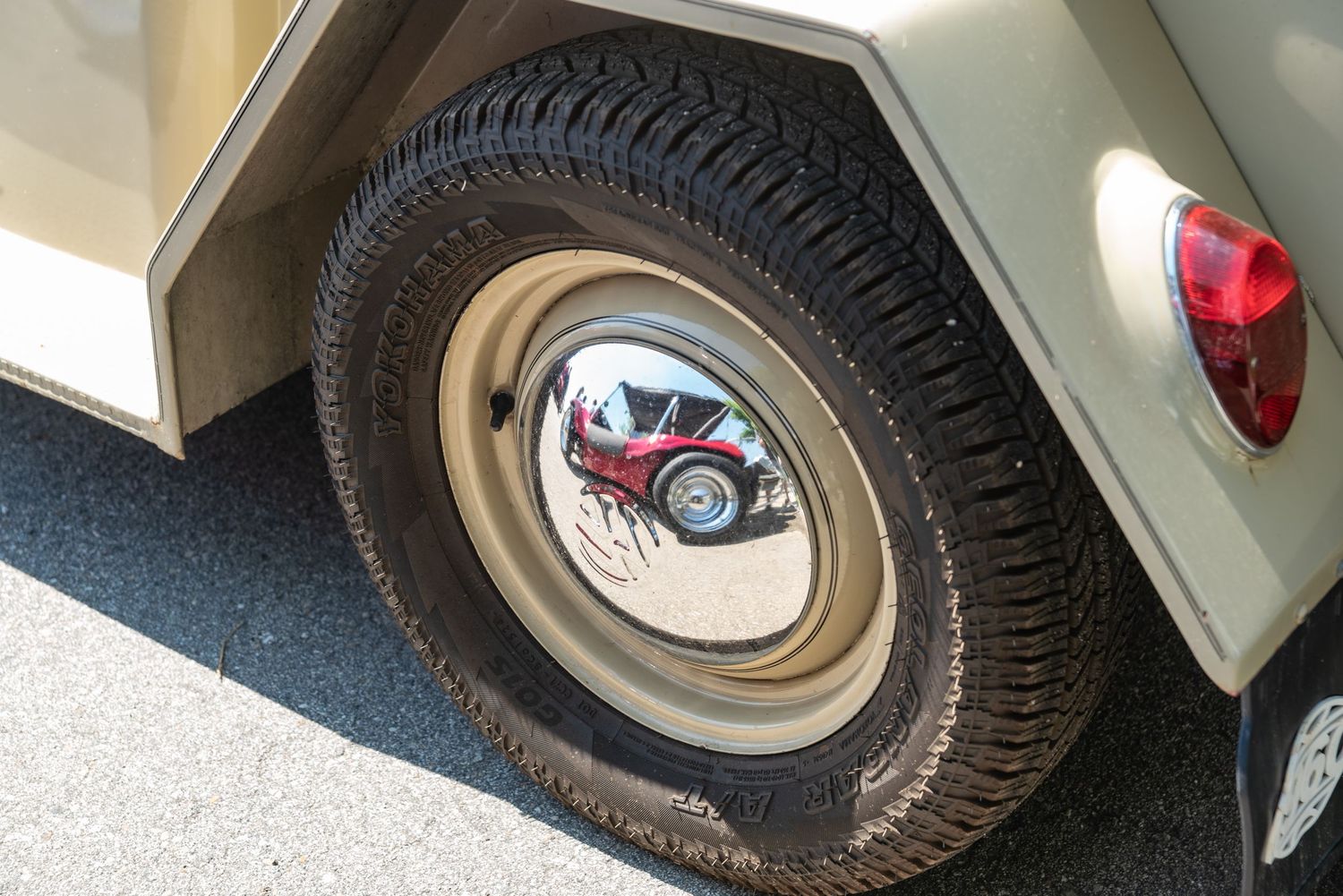 Close-up of a vintage vehicle tire with a chrome hubcap reflecting a classic red car at an outdoor auto show.