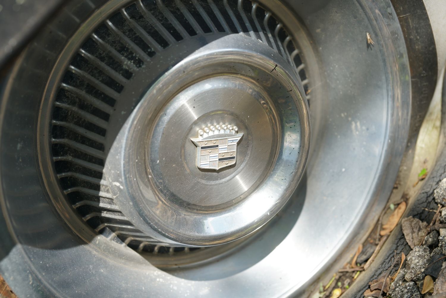 Vintage Cadillac hubcap with emblem detail on an old classic car wheel, showing signs of age and wear.