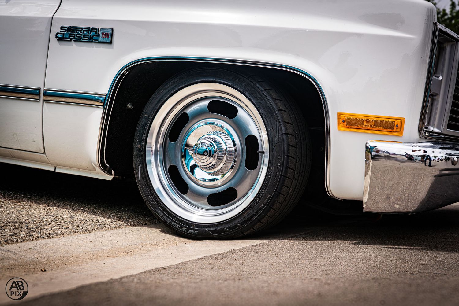 Chrome rally wheel on a lowered white classic Chevrolet truck at a car show.