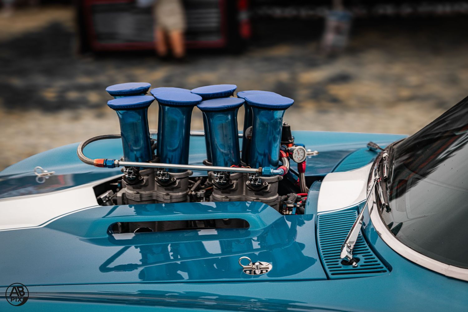 Blue classic car with quad velocity stack carburetors on engine, hood open at car show.