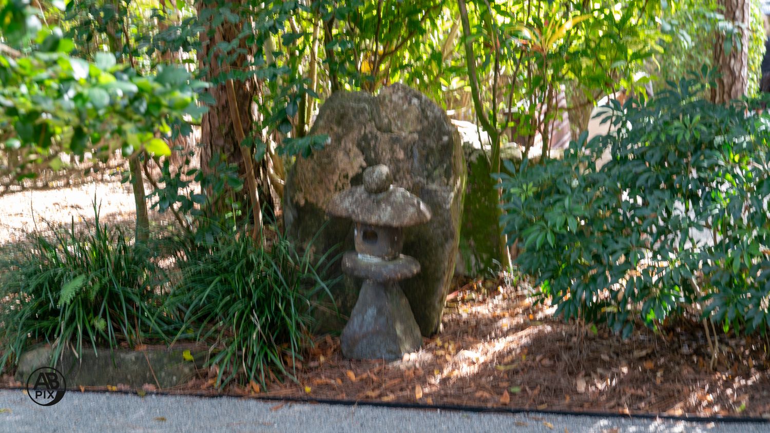 Stone lantern garden ornament nestled among lush green shrubs and trees in a Japanese garden.