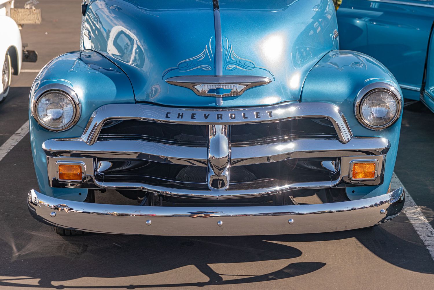 Vintage blue Chevrolet truck front view showcasing chrome grille, dual headlights, and classic 1950s styling at a car show.