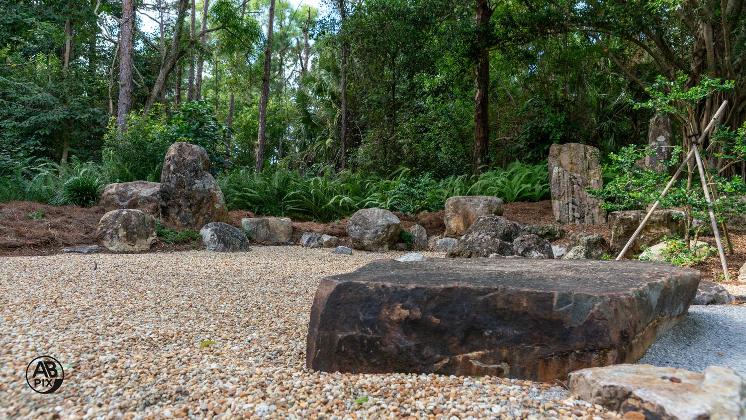 Flat natural stone slab surrounded by gravel and scattered boulders in a Japanese-inspired garden landscape.